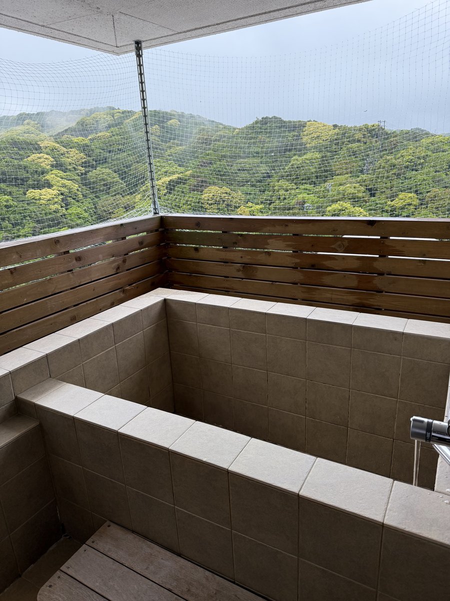 An open-air bath on a balcony with a wooden screen, overlooking green hills