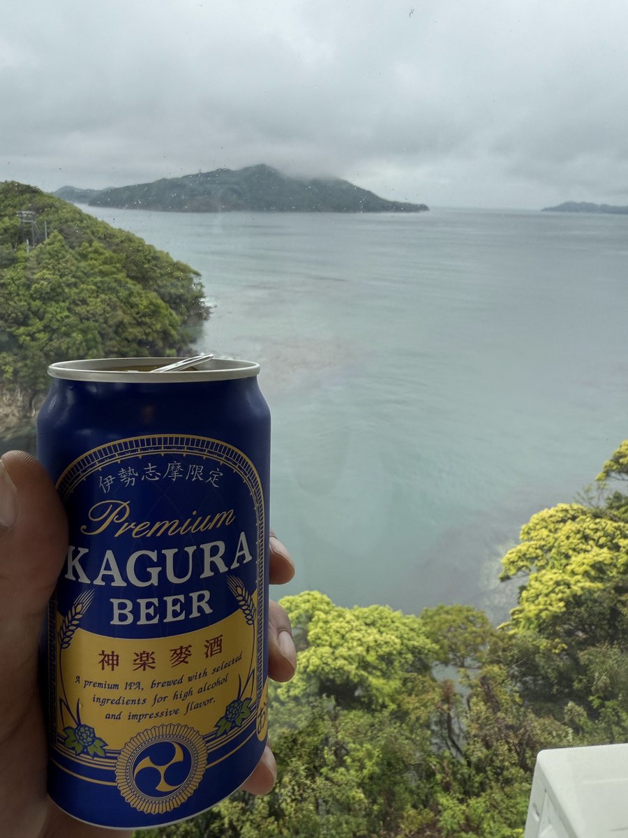 A can of Kagura beer held up in front of a view of green islands in a misty bay