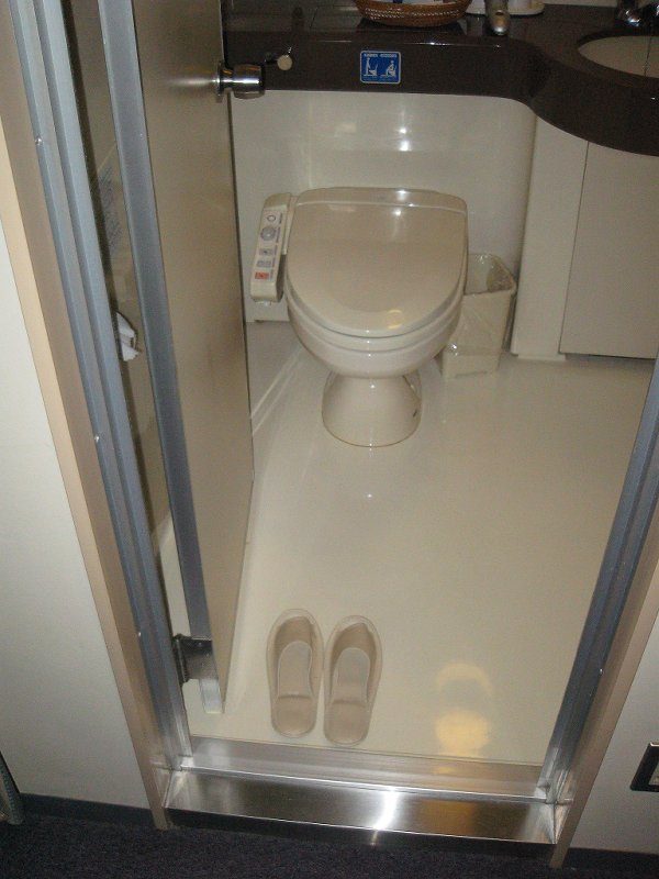 A small toilet room with a pair of toilet slippers set out just inside the door