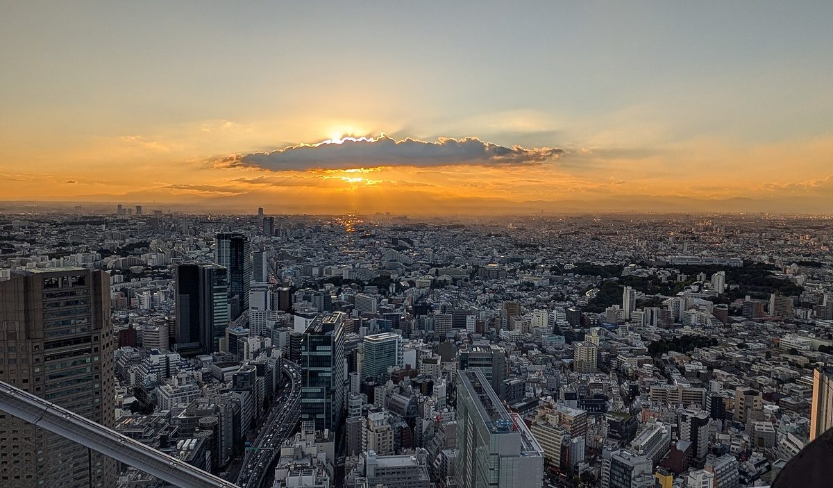 The sun setting behind a cloud over a sea of buildings, seen from the SHIBUYA SKY rooftop