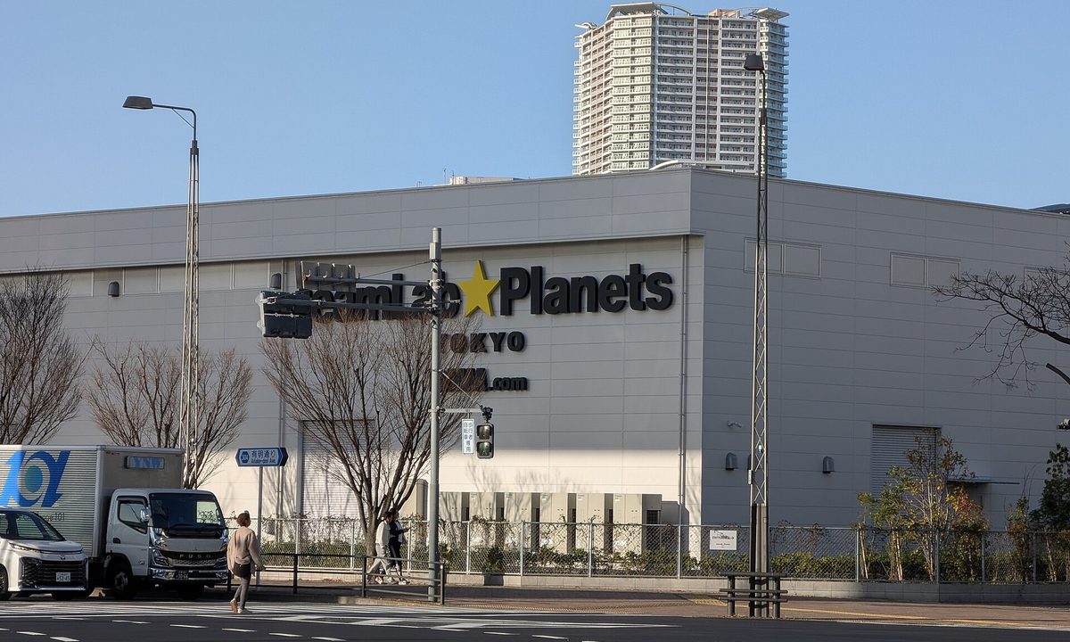 The large grey building of teamLab Planets TOKYO in Toyosu (Tokyo) with its logo on the wall, seen across a wide street