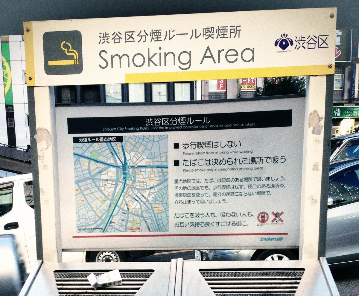 A public smoking area sign in Shibuya (Tokyo) with a map and the words Smoking Area, above two stand ashtrays