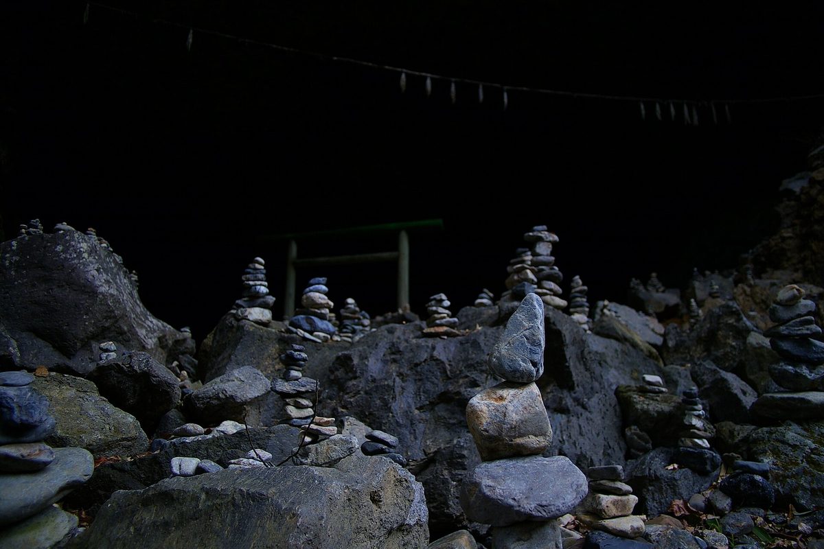 Inside the dark Amano Yasukawara cave, with countless small stacks of stones on the rocky floor