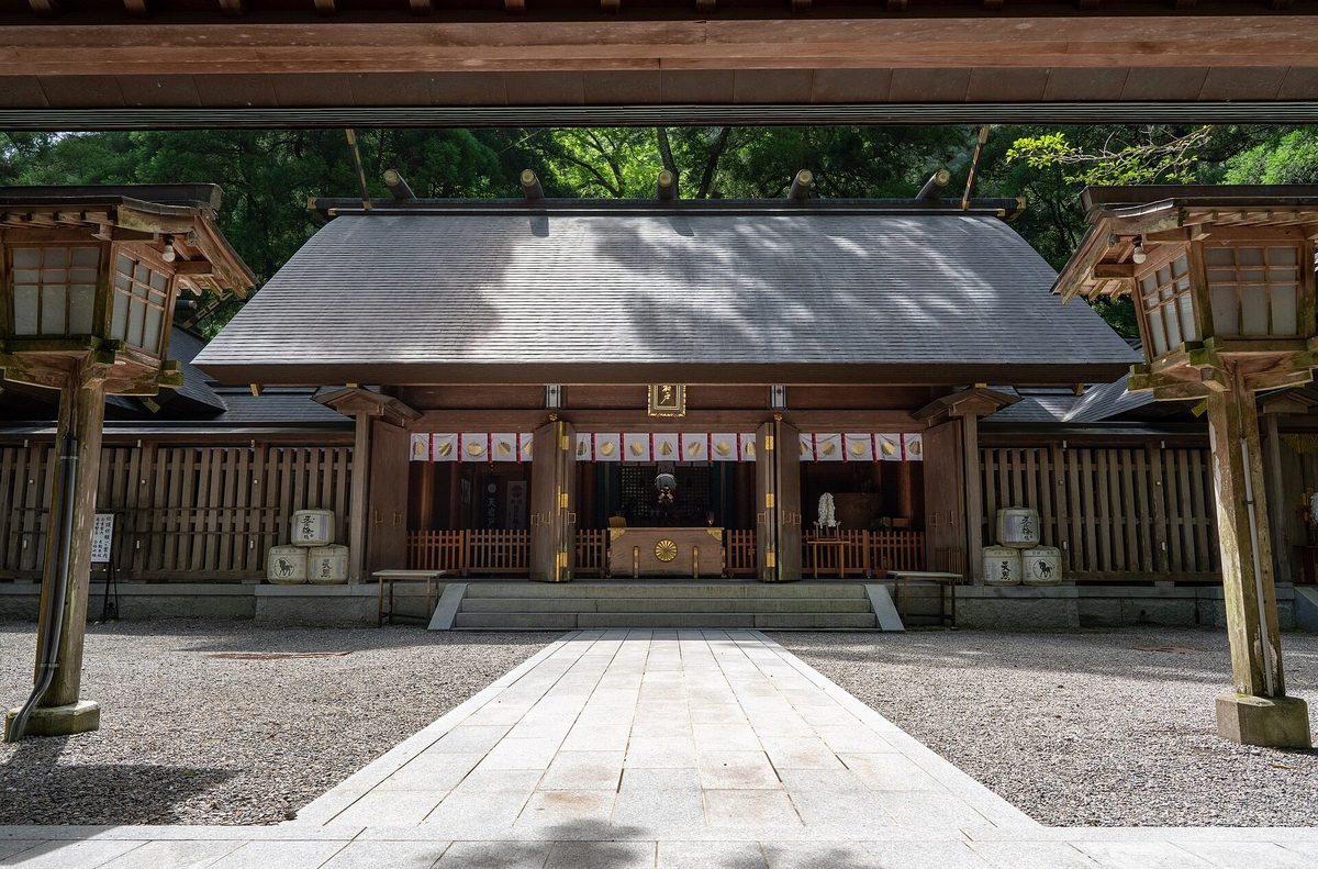 The wooden worship hall of Amanoiwato Shrine's West Shrine in Takachiho, seen across a gravel courtyard between two stone lanterns