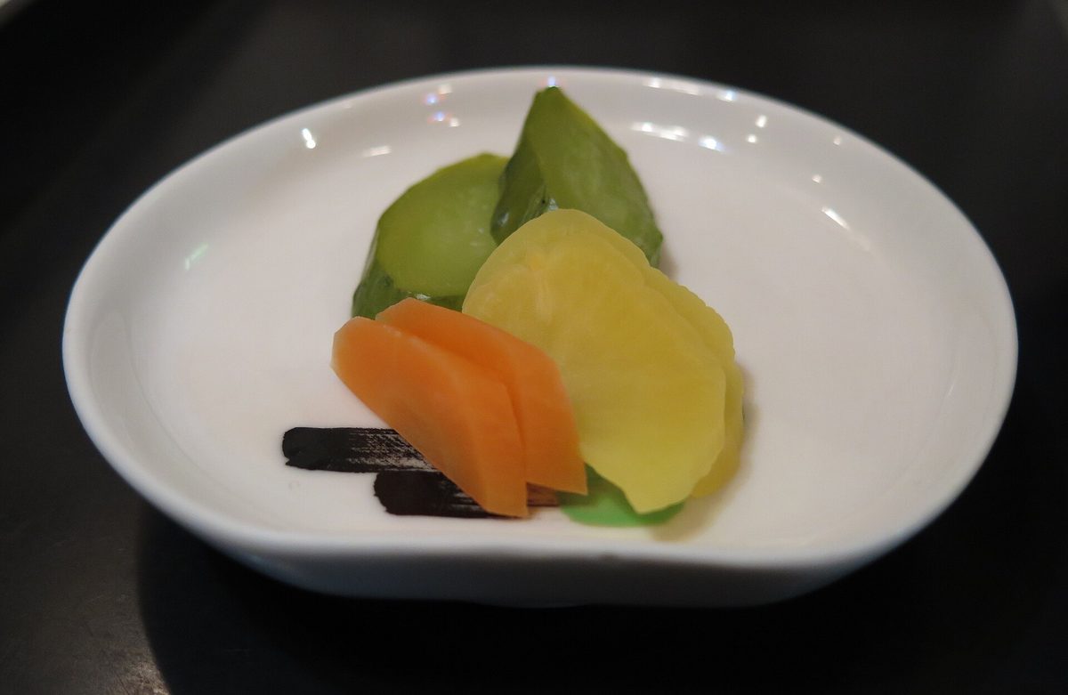 A small white dish of Japanese pickles: yellow takuan, orange carrot and green cucumber slices