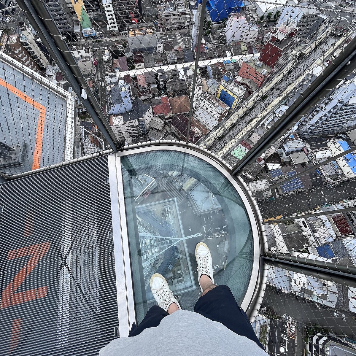 Looking down at the city streets through the see-through floor at the tip of a deck high on Tsutenkaku Tower