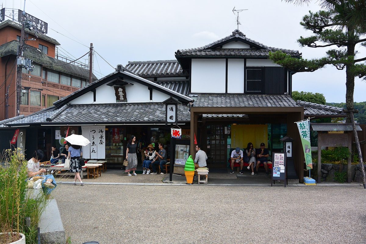 有瓦屋頂和暖簾的傳統兩層木造茶店，門前有幾位遊客