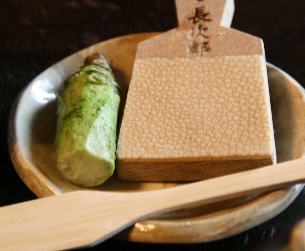 A fresh green wasabi root beside a small wooden sharkskin grater on a plate