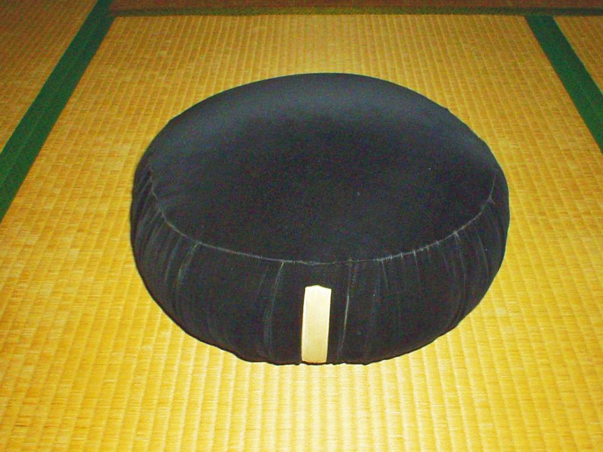 A round black zafu meditation cushion on a tatami mat