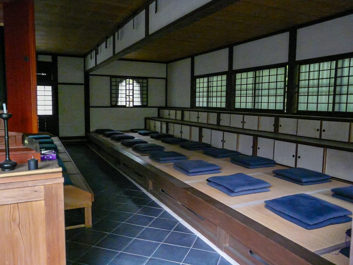 An empty zazen hall with rows of blue cushions on raised wooden platforms at Enko-ji temple